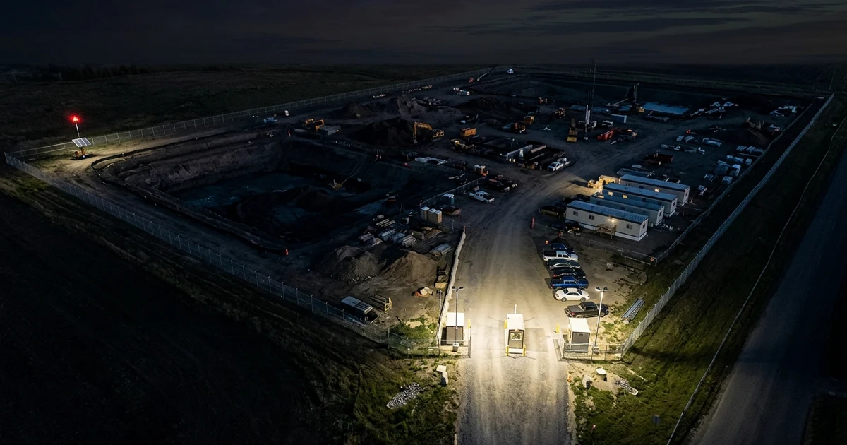 Photorealistic aerial photo of construction site at night showing dark unlit perimeter fence gaps with solar camera trailer in distance
