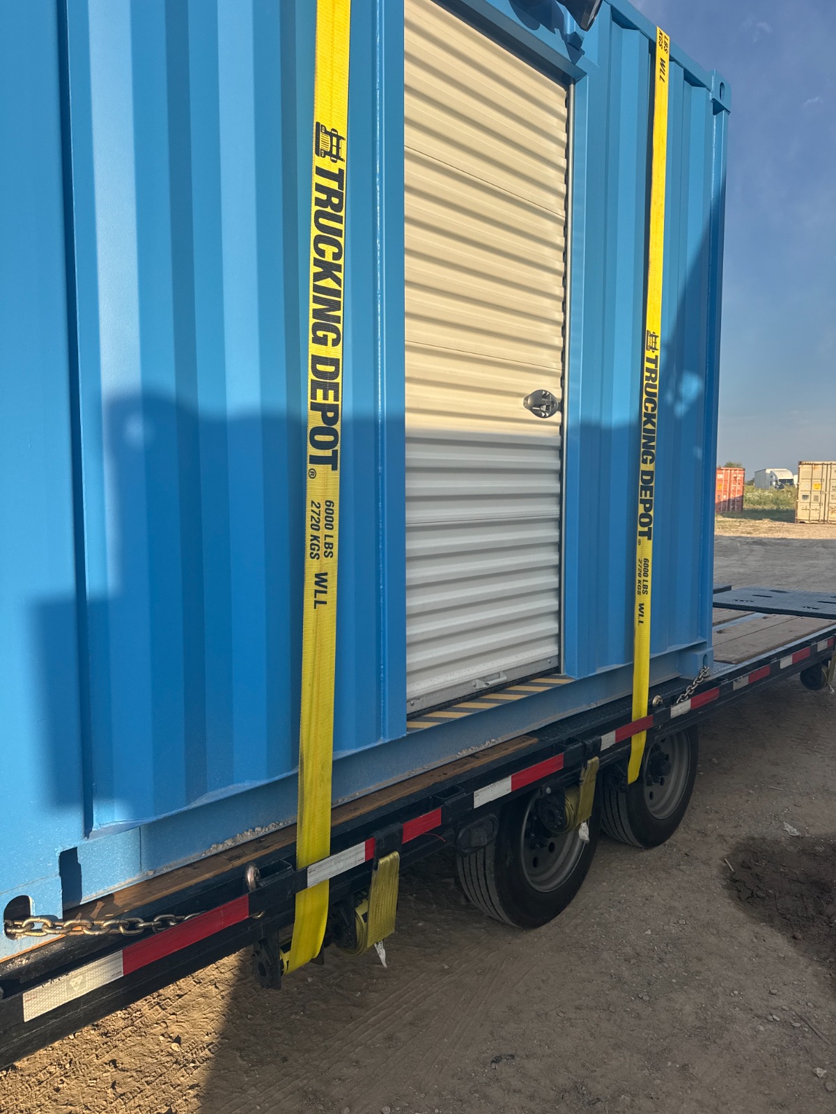 Close-up of a blue 10-foot shipping container turnstile checkpoint secured with bright yellow cargo straps on a flatbed trailer