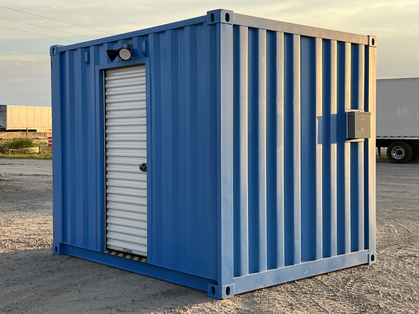 Angled exterior view of a blue 10-foot shipping container turnstile checkpoint with a closed white roll-up door and side junction box