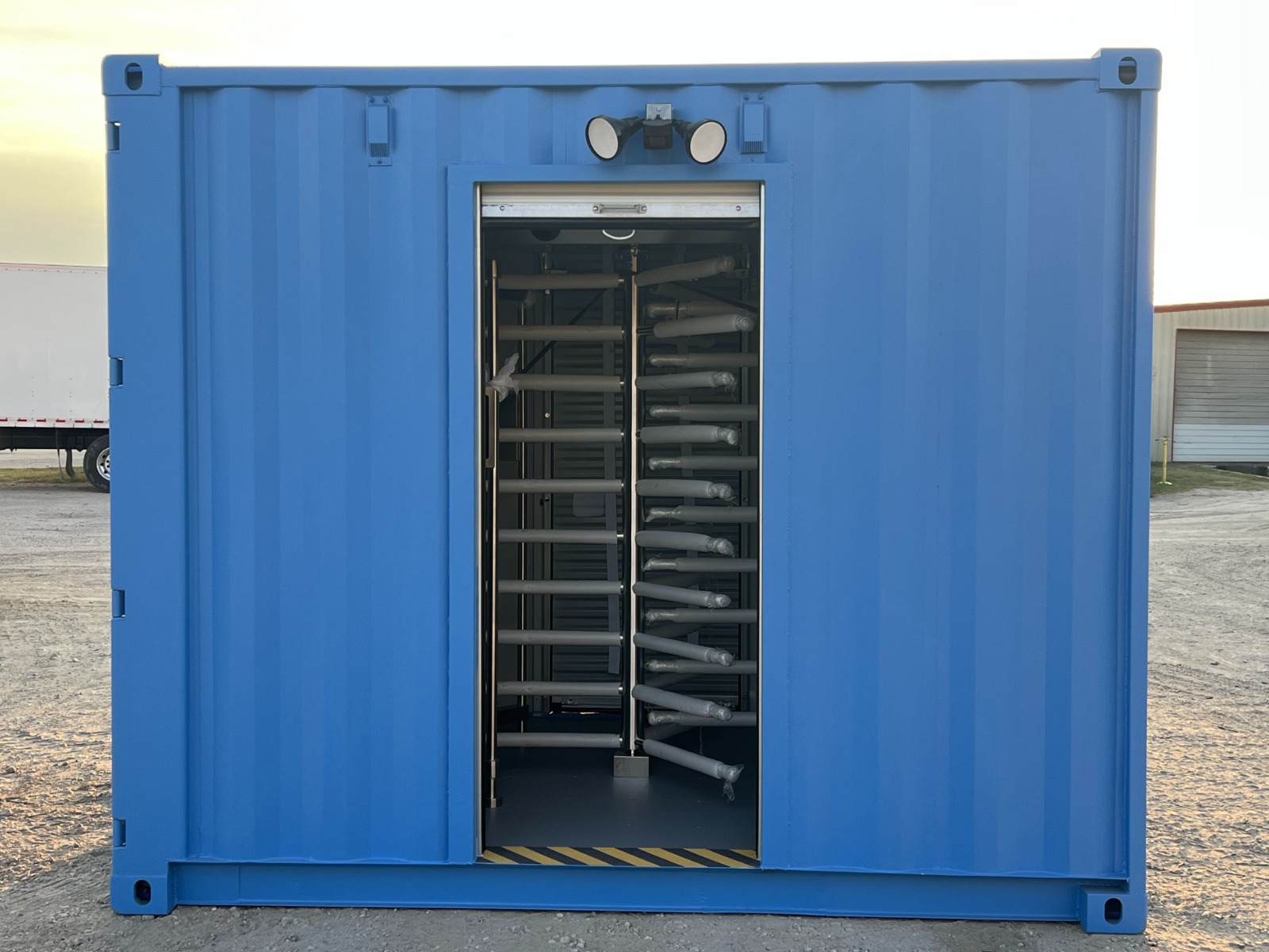 Straight-on landscape view of a blue 10-foot shipping container turnstile checkpoint with an open roll-up door showing internal turnstile bars