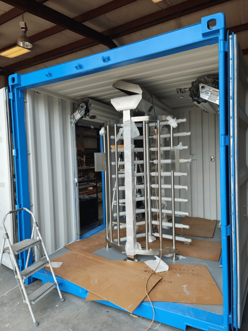 Interior view of a full-height stainless steel turnstile and roll-up security doors inside a 10-foot shipping container checkpoint